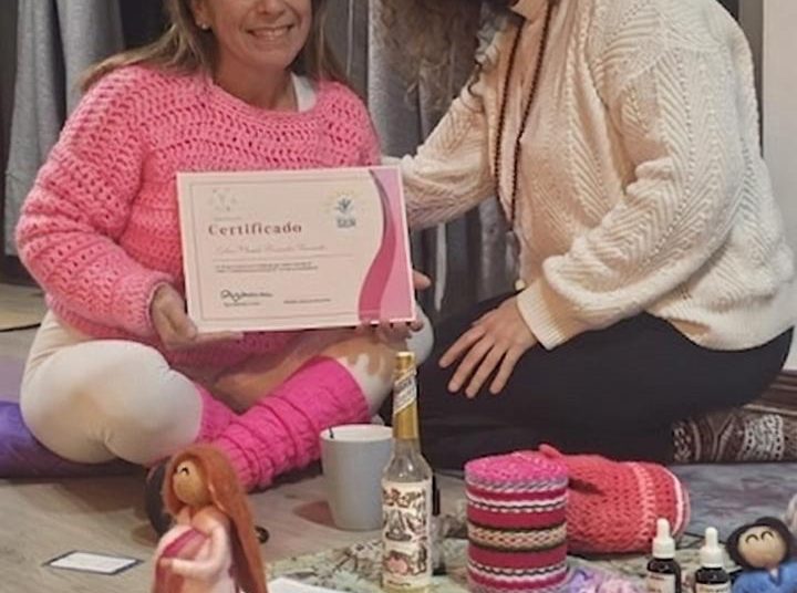Eyleen Fernandez, directora de Equicentro, sentada en el suelo sonriendo y sosteniendo su certificado de Doula de Centro Ser junto a su instructora y elementos de terapia perinatal.