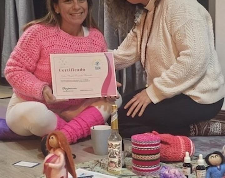 Eyleen Fernandez, directora de Equicentro, sentada en el suelo sonriendo y sosteniendo su certificado de Doula de Centro Ser junto a su instructora y elementos de terapia perinatal.
