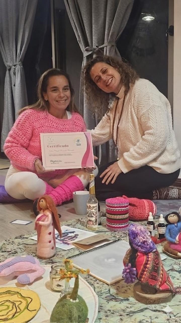 Eyleen Fernandez, directora de Equicentro, sentada en el suelo sonriendo y sosteniendo su certificado de Doula de Centro Ser junto a su instructora y elementos de terapia perinatal.